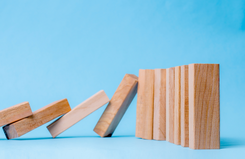 Wooden dominoes lined up with half falling down in a chain reaction
