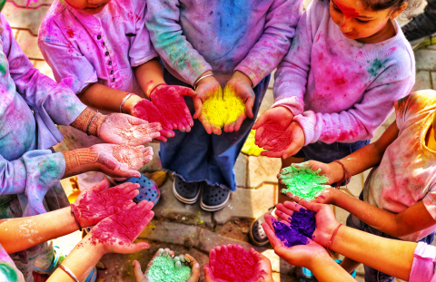 Aerial view of children holding hands toward the center of a circle, everyone holding pigment in their hands