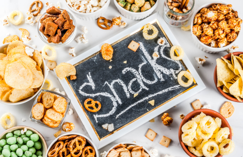 Bowls of different snacks surround a small black board with Snacks written on it