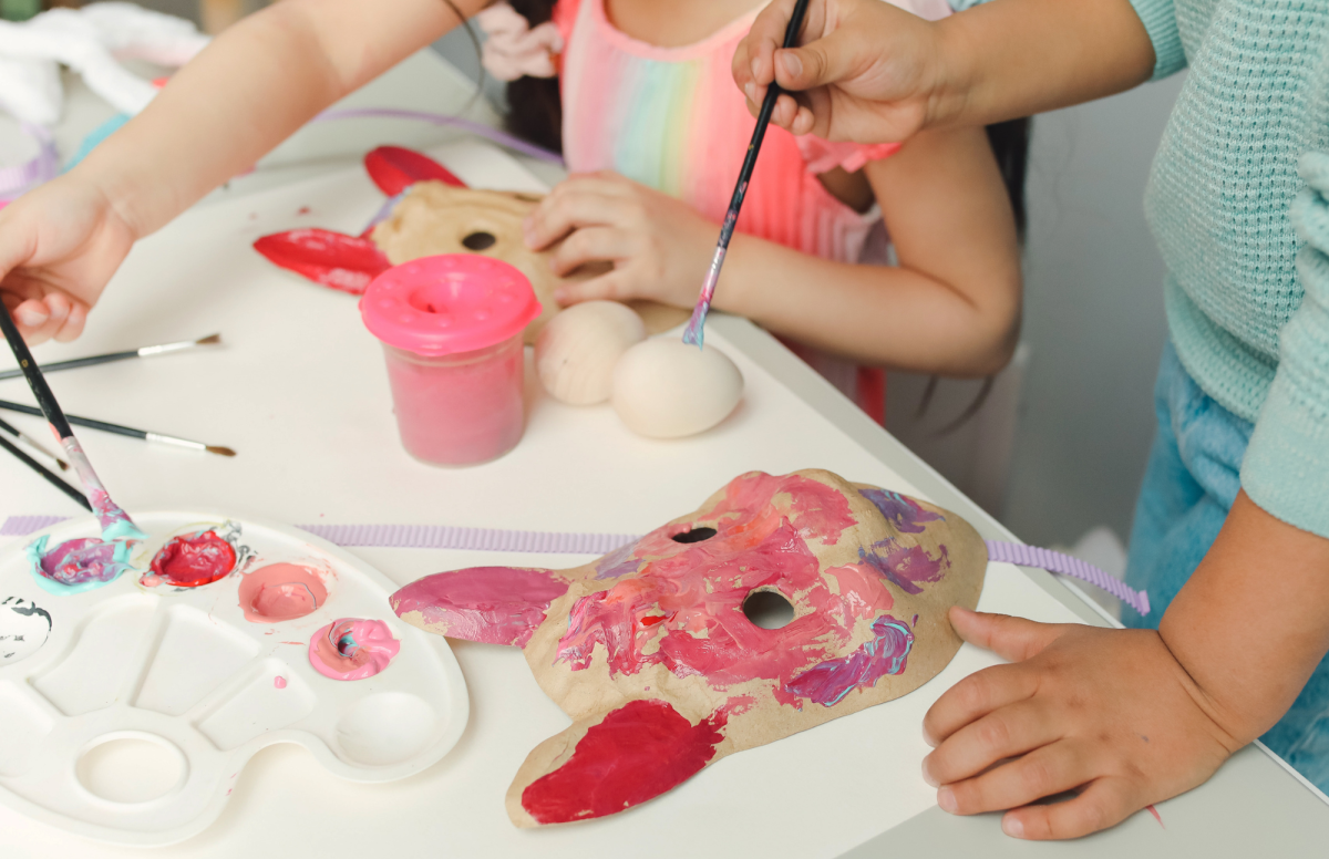 Two kids painting masks to look like pigs.