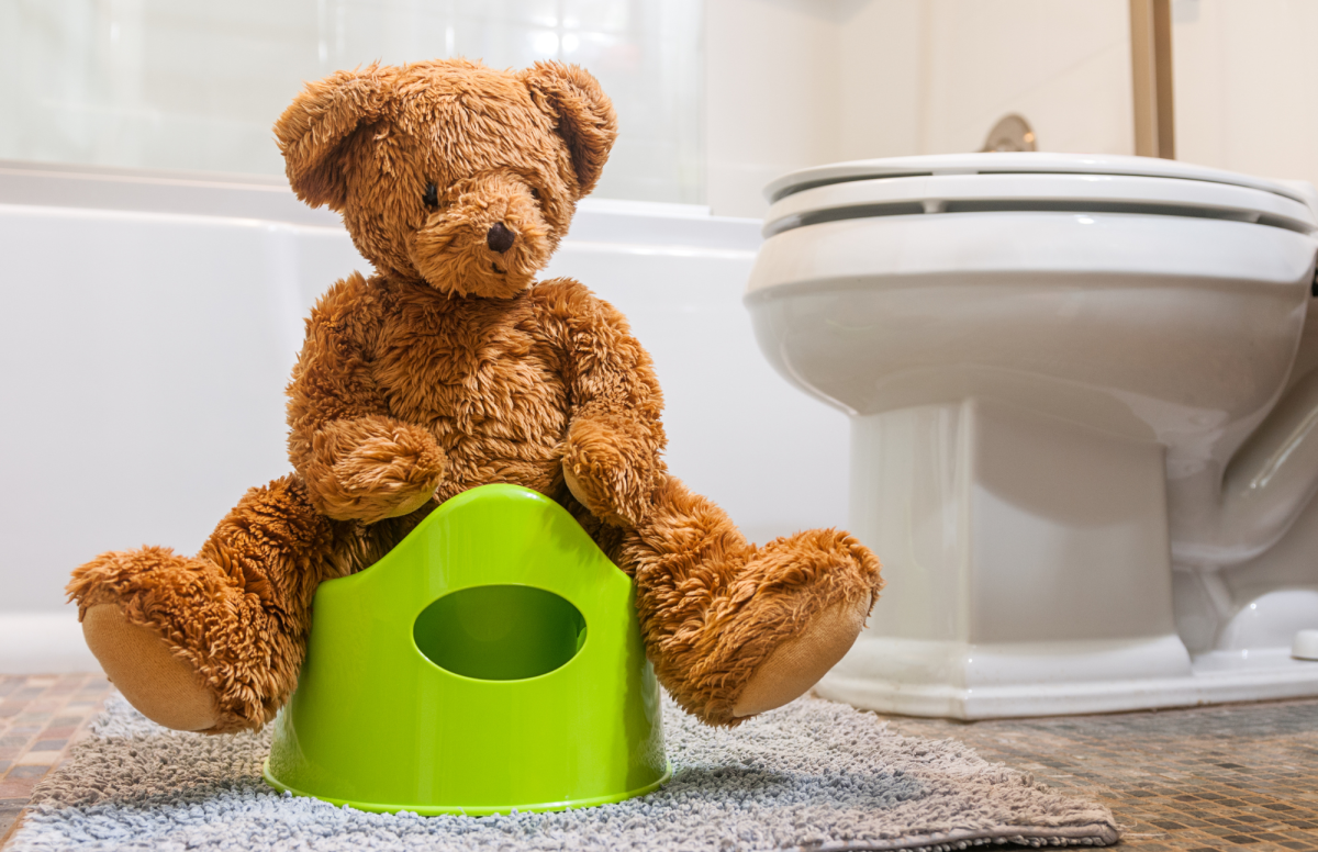 Cute little brown teddy bear straddles atop a bright green kiddy potty in a white bathroom