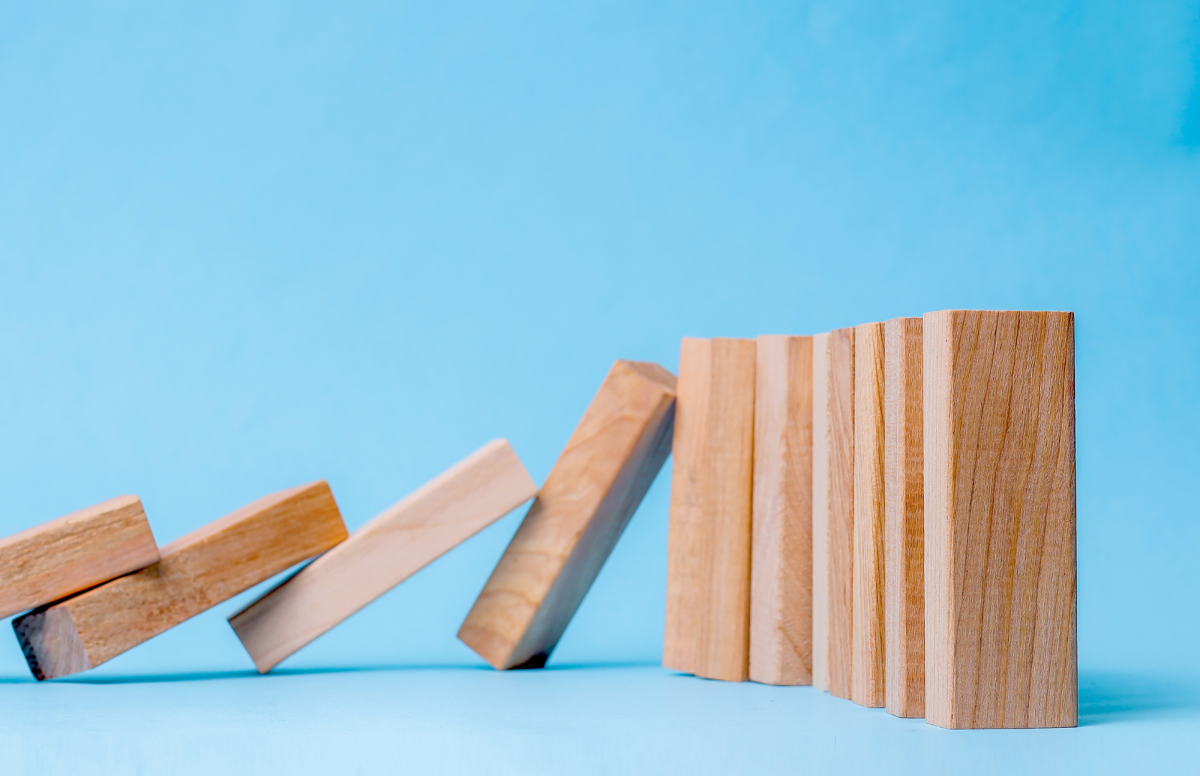 Wooden dominoes lined up with half falling down in a chain reaction