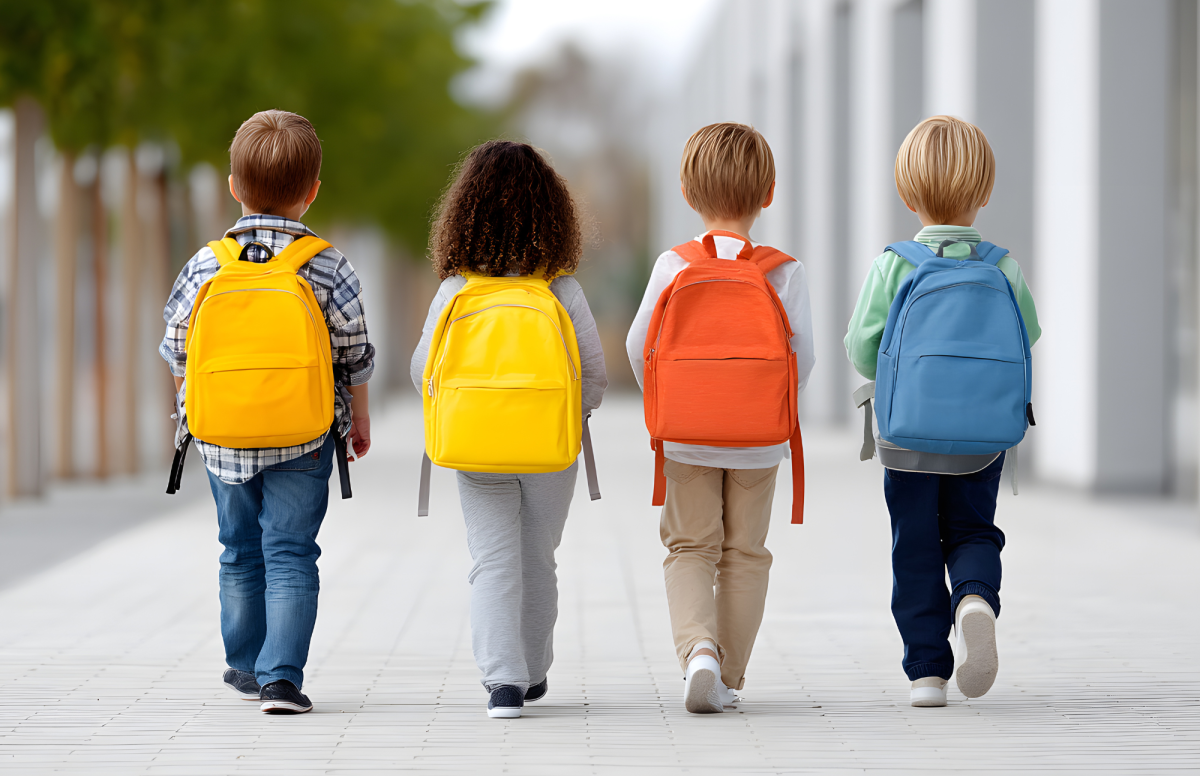Four young kids wearing backpacks walking in a line away from the camera.