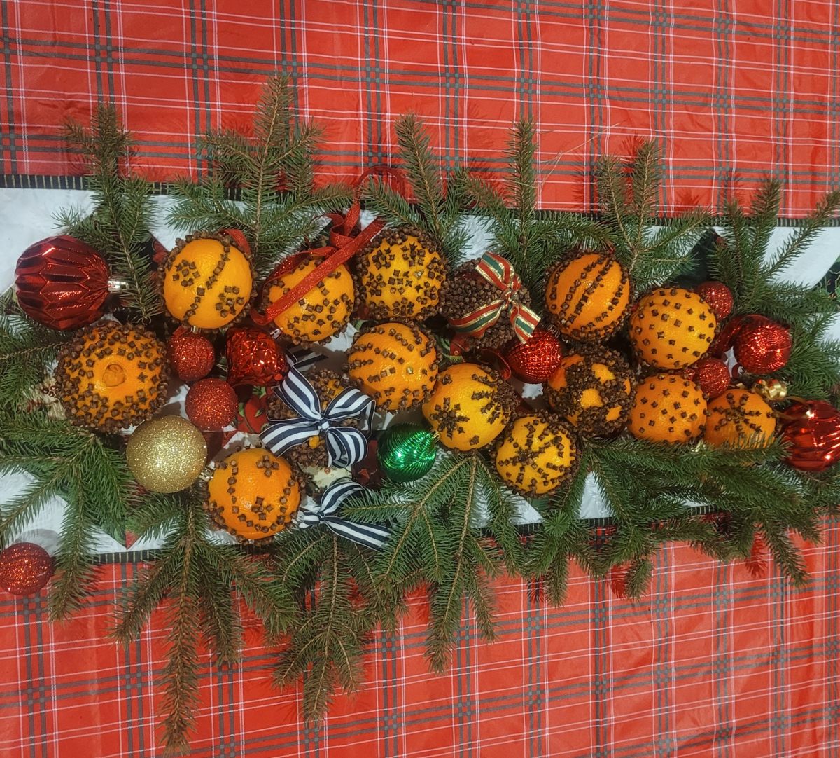 many oranges with cloves pressed into them in varying designs while surrounded by pine twigs
