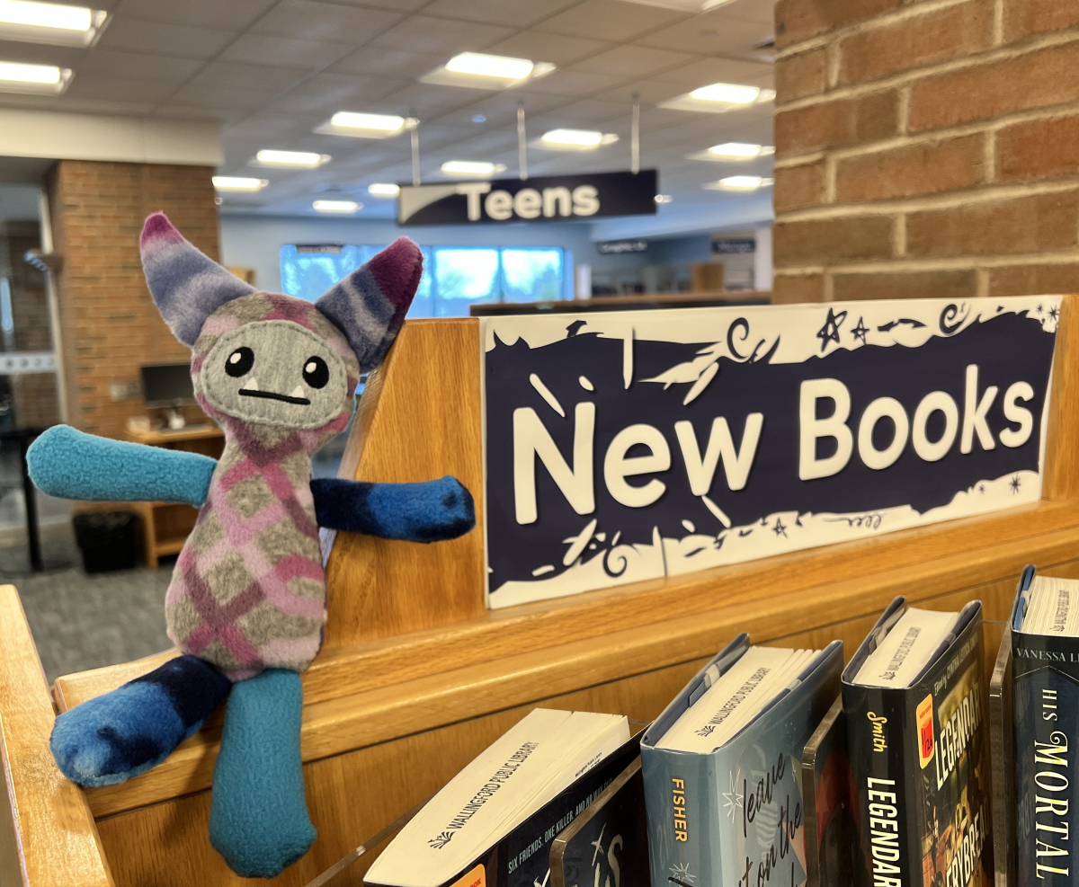 A blue and purple cute monster plushie sitting with new library books.